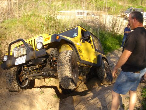 2002 Jeep Wrangler - A man watches as a yellow Jeep Wrangler navigates a challenging off-road terrain with other vehicles nearby.