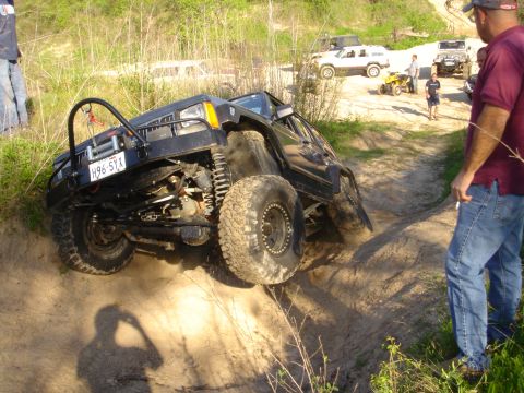 2002 Jeep Wrangler - A modified Jeep Cherokee XJ navigates an off-road trail with other vehicles and people in the background.