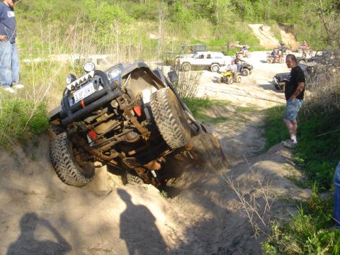 2002 Jeep Wrangler - A Jeep Wrangler is seen tilted on its side while navigating a challenging off-road trail, with other vehicles and spectators present.