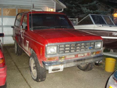 1985 Ford Bronco II - A red 1985 Ford Bronco II is parked in front of a garage and a boat.