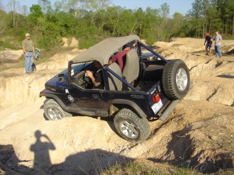 2002 Jeep Wrangler - A dark blue Jeep Wrangler tackles a challenging off-road course with multiple people observing.