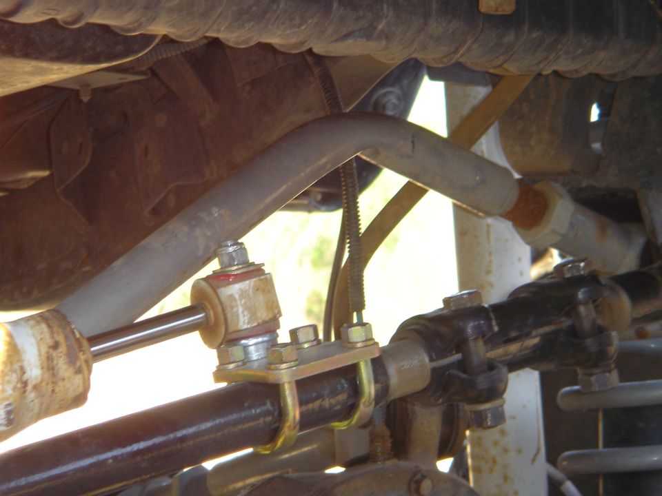Underbody view of steering stabilizer in poly bushing clamped to axle with gold U-bolts