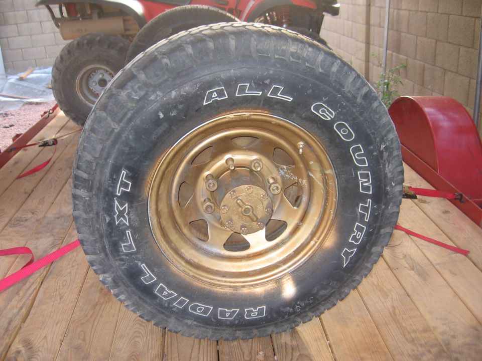 All Country Radial LXT tire on gold 8-lug steel wheel with locking hub, lying on wood trailer deck