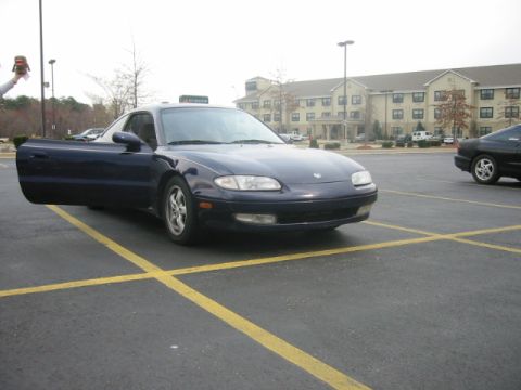 1993 Ford Probe - Dark blue coupe with driver's door ajar, parked in a lot with a hotel in the background.