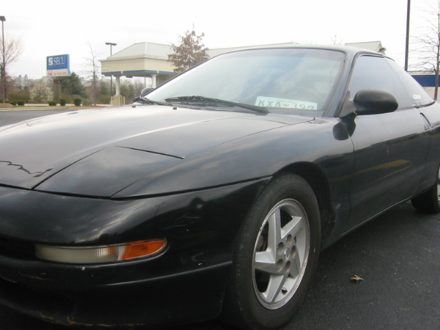 Black second-generation Ford Probe with faded hood paint and alloy wheels in a parking lot
