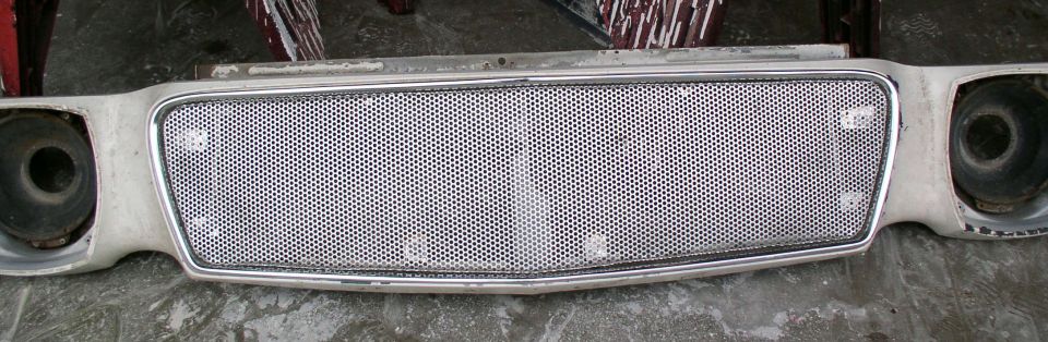 Car grille with a honeycomb pattern and chrome trim, showing headlight openings on either side