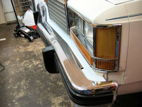 1985 Ford LTD Crown Victoria - Close-up of a car's front bumper and headlight assembly, revealing chrome detailing and an amber turn signal light.