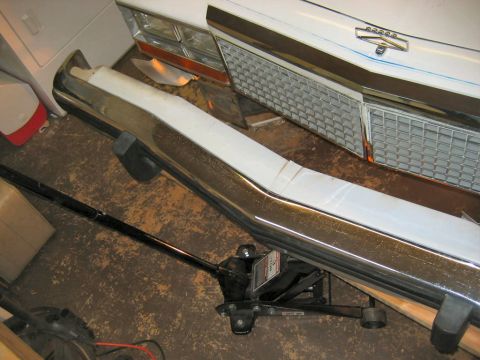 1985 Ford LTD Crown Victoria - A chrome bumper and grille are shown, supported by a floor jack.