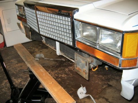 1985 Ford LTD Crown Victoria - Front view of a white 1985 Ford Crown Victoria LTD with its bumper removed, resting on a jack.