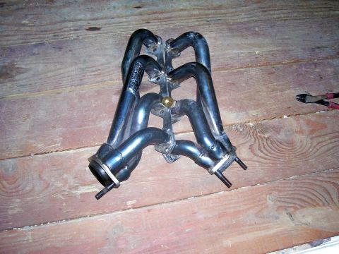 1991 Ford Bronco - An exhaust manifold is shown on a wooden floor, with pliers visible in the background.