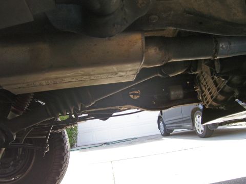 1991 Ford Bronco - The underside of a vehicle, focusing on the exhaust system and suspension, with another car in the background.