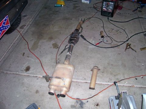 1991 Ford Bronco - Exhaust system part laid out on a garage floor with welding equipment nearby.