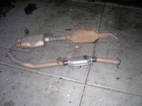 1991 Ford Bronco - Two exhaust system components, likely a muffler and a catalytic converter, are shown on a concrete surface.