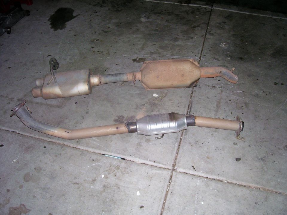 Old exhaust muffler section next to a pipe fitted with a new high-flow catalytic converter