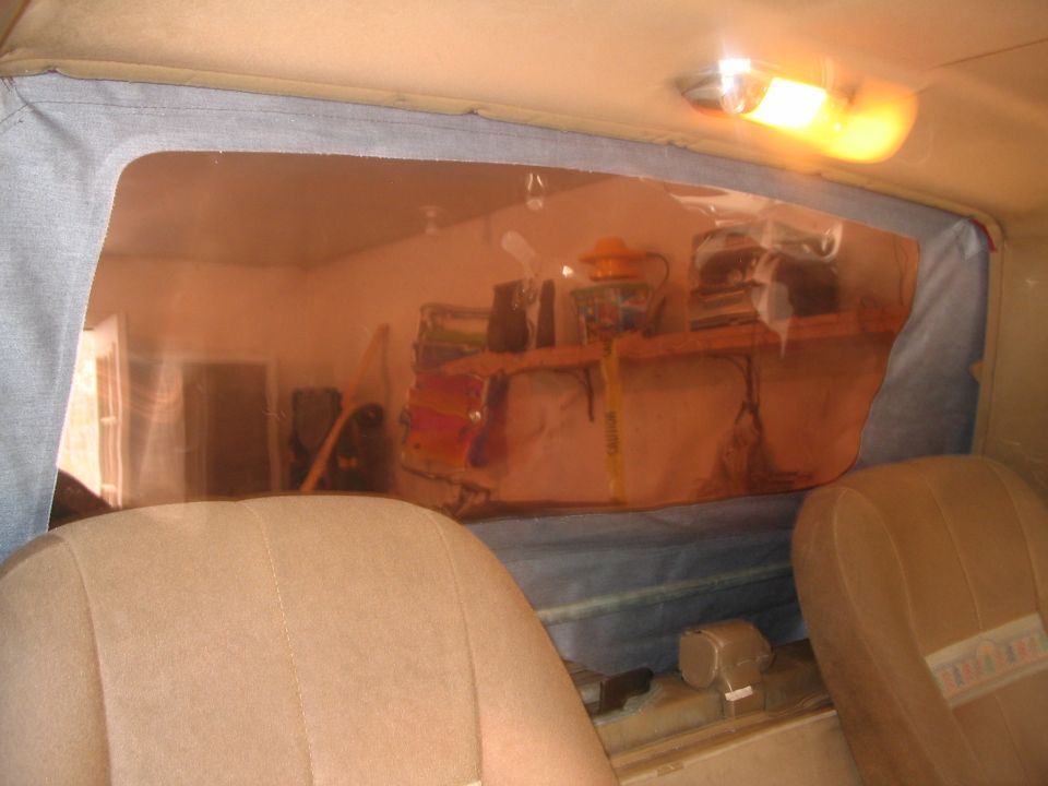 Interior of a vehicle with tan seats and a clear plastic rear window showing a cluttered shelf