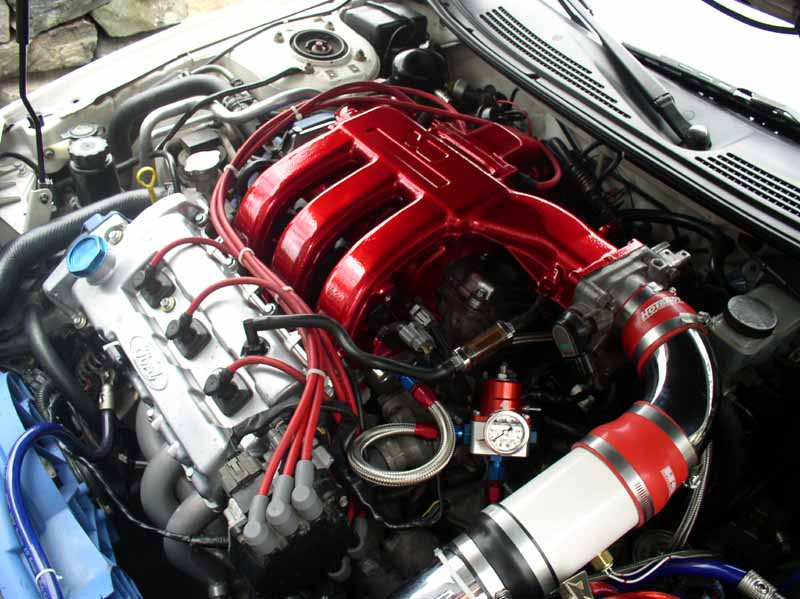 Engine bay with red intake manifold and silver valve cover. "Ford" logo visible on valve cover