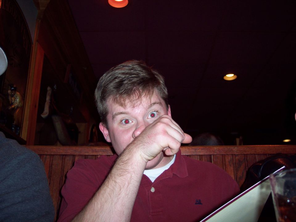 Man in a maroon polo shirt with his hand over his face, looking at the camera