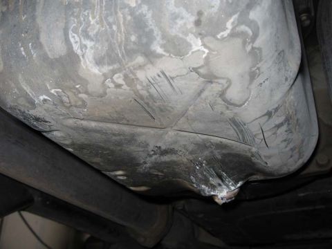 2000 Jeep TJ - The underside of a vehicle's fuel tank displays significant damage, including dents and scrapes.