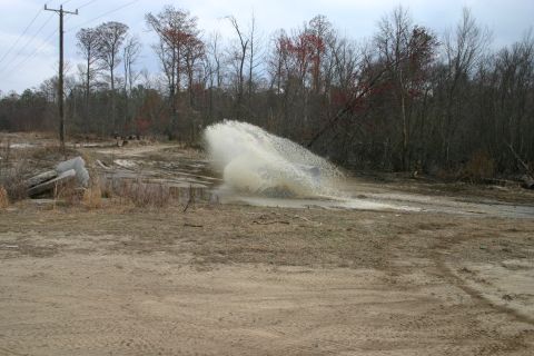 1989 Ford Bronco - An SUV drives through a muddy puddle, creating a large water splash.