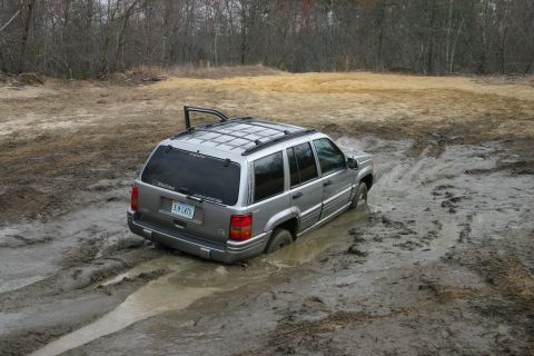 1989 Ford Bronco - A silver SUV is deeply stuck in thick mud, with its rear end partially submerged.