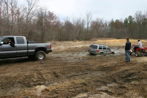 1989 Ford Bronco - A group of vehicles navigates a muddy off-road course, with one SUV deeply stuck in the mire.