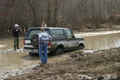 1989 Ford Bronco - A Ford Bronco is stuck in a muddy ditch with people observing the situation.