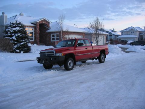 1996 Dodge 2500 - A red 1996 Dodge 2500 pickup truck is parked on a snowy street in front of a suburban house.