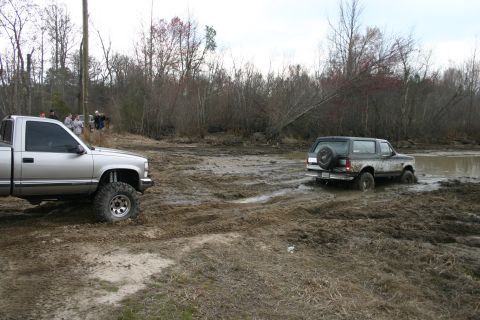 1989 Ford Bronco - A Ford Bronco is stuck in the mud while a silver pickup truck waits nearby.