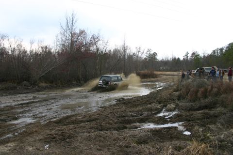 1989 Ford Bronco - A 1989 Ford Bronco navigates a muddy off-road course, kicking up water and mud.