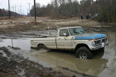 1989 Ford Bronco - This Ford F-Series pickup truck is stuck in a mud puddle with another vehicle visible in the background.