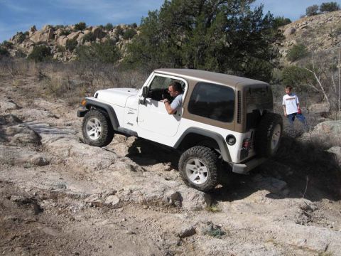 2000 Jeep TJ - A white Jeep TJ navigates a rocky trail under a clear blue sky.