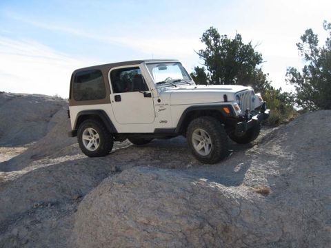 2000 Jeep TJ - A white Jeep Wrangler with a brown hardtop navigates a rocky, off-road landscape under a clear sky.