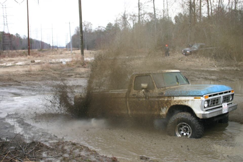 Muddy 1973 Ford F-Series truck splashing through a mud pit, another vehicle visible in background