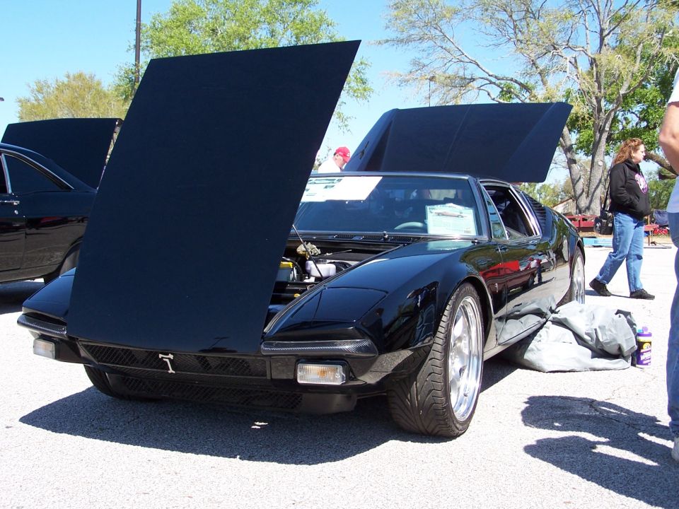 Black De Tomaso Pantera-style sports car at car show with front clamshell hoods raised
