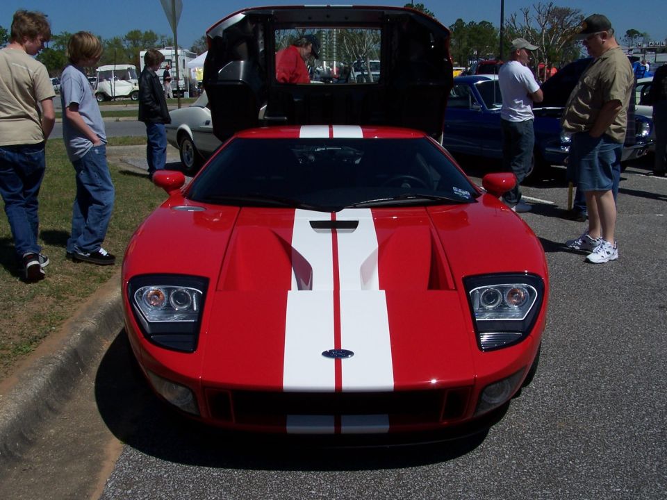Red Ford GT with white racing stripes, front view, rear hatch open at a car show
