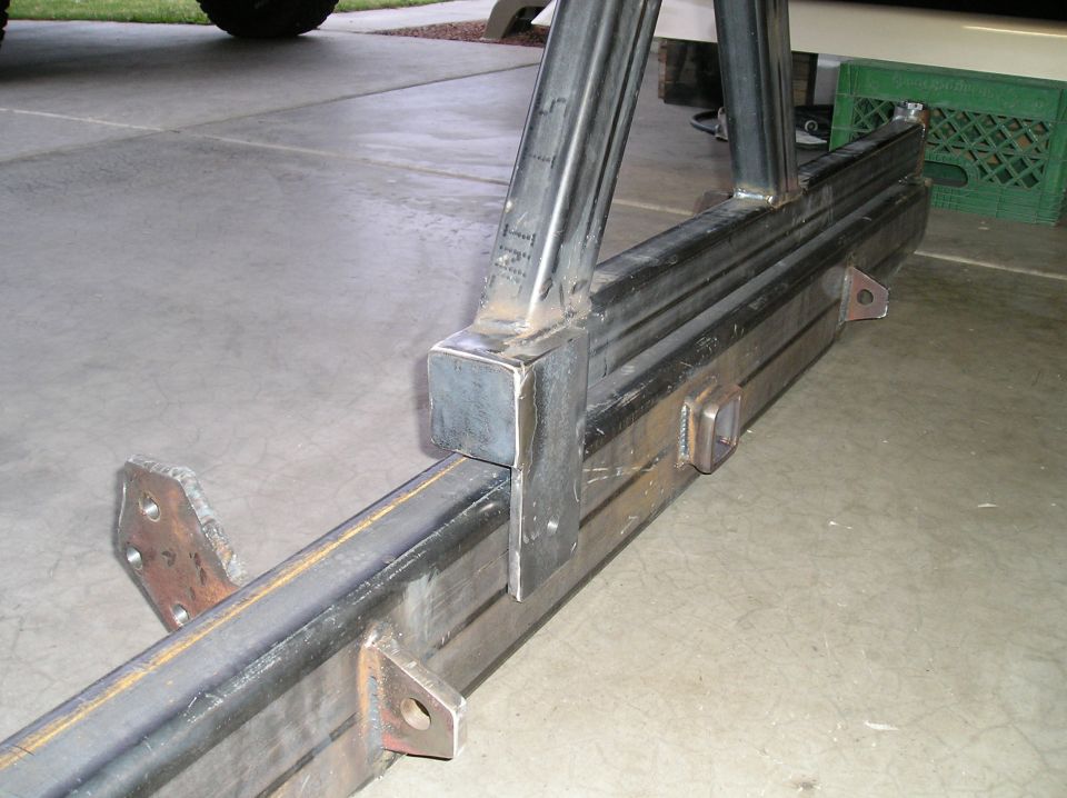 Bare welded steel custom bumper with drilled mounting tabs on a garage floor