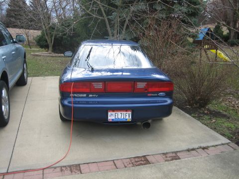 1995 Ford Probe - The rear of a blue 1995 Ford Probe is visible, parked on a concrete driveway next to another vehicle.