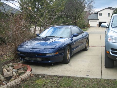 1995 Ford Probe - A blue 1995 Ford Probe is parked in a driveway, with a silver SUV to its right.