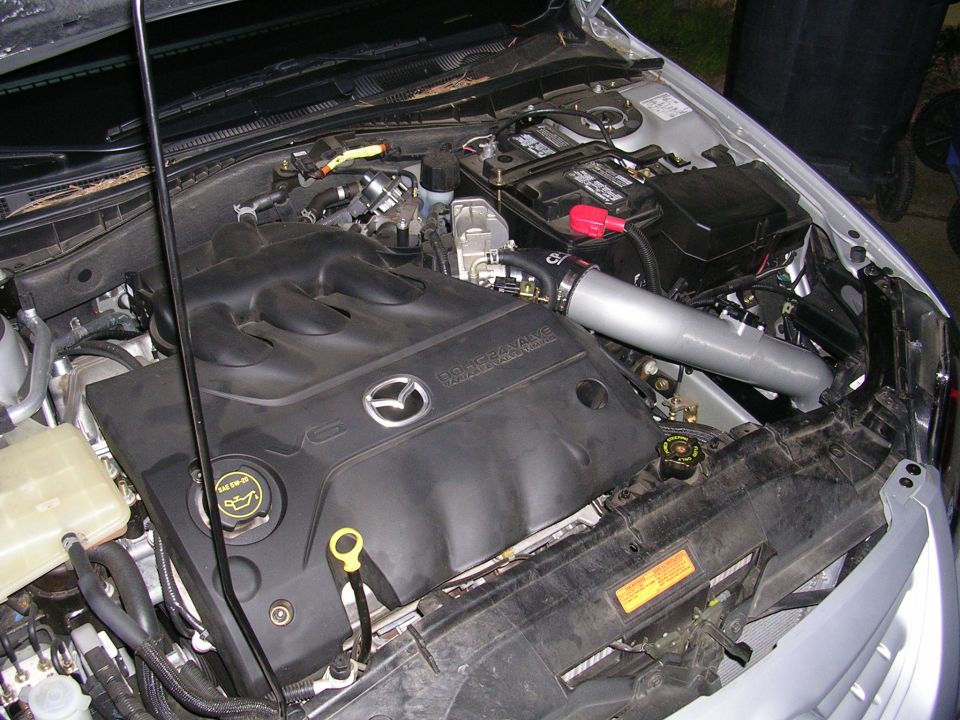 Mazda engine bay with V6 badge and aftermarket intake pipe