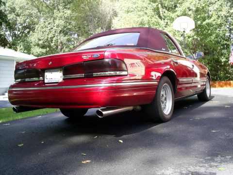 1995 Ford Crown Victoria - A red convertible sedan with a maroon top is shown from the rear quarter angle on a paved driveway.