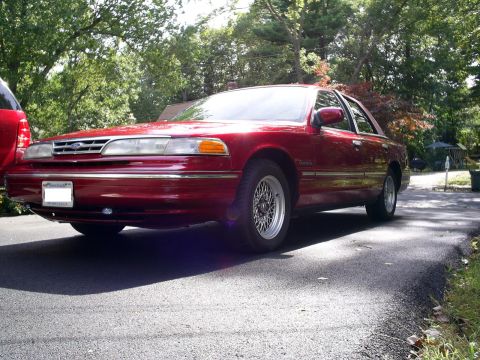 1995 Ford Crown Victoria - A red 1995 Ford Crown Victoria sedan is viewed from a three-quarter front angle on a sunny day.