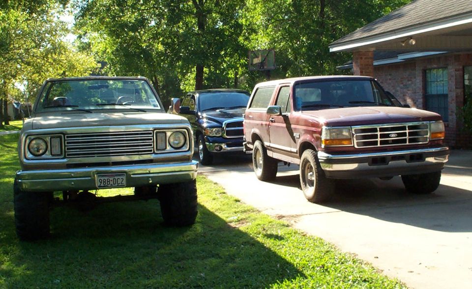 Lifted tan Dodge pickup, blue Ram and dark red Ford Bronco parked in a yard
