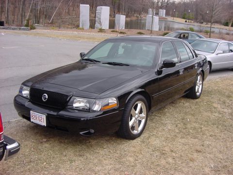 1995 Ford Crown Victoria - This black sedan features a distinctive black grille and chrome wheels, with other vehicles visible in the background.