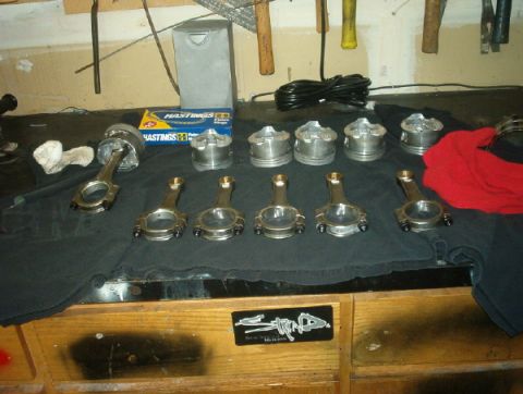 1994 Mazda MX-3 - Engine parts, including pistons and connecting rods, are arranged on a workbench next to a box of piston rings.