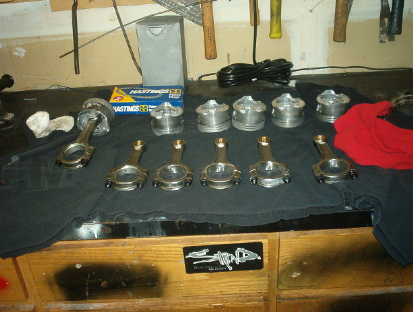Engine pistons and connecting rods laid out on a black cloth, with a box of Hastings piston rings