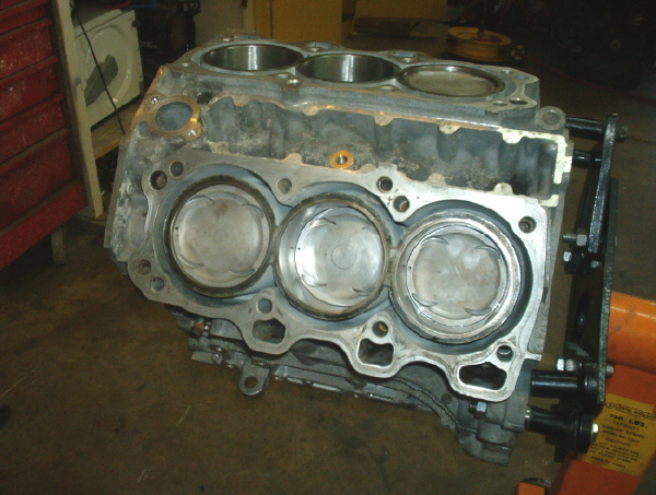 Engine block with three visible pistons, mounted on an orange engine stand
