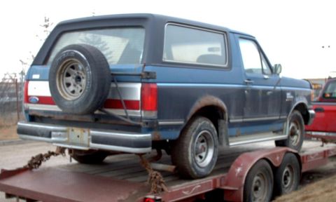 1990 Ford Bronco - A blue 1990 Ford Bronco is seen on a trailer, a rear-mounted spare tire and a distinctive body style.