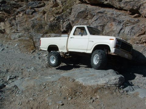 1981 Ford F-150 - A lifted white pickup truck navigates a rocky terrain, its off-road capabilities.