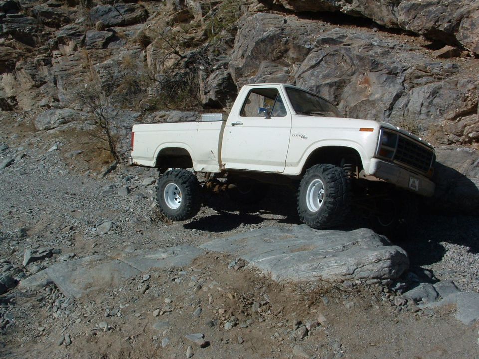 White pickup truck with lifted suspension and large tires driving on a rocky, off-road trail