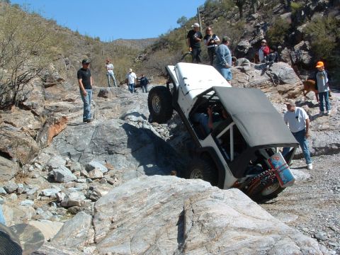 1981 Ford F-150 - A white Jeep Wrangler navigates a challenging rocky terrain with several onlookers present.